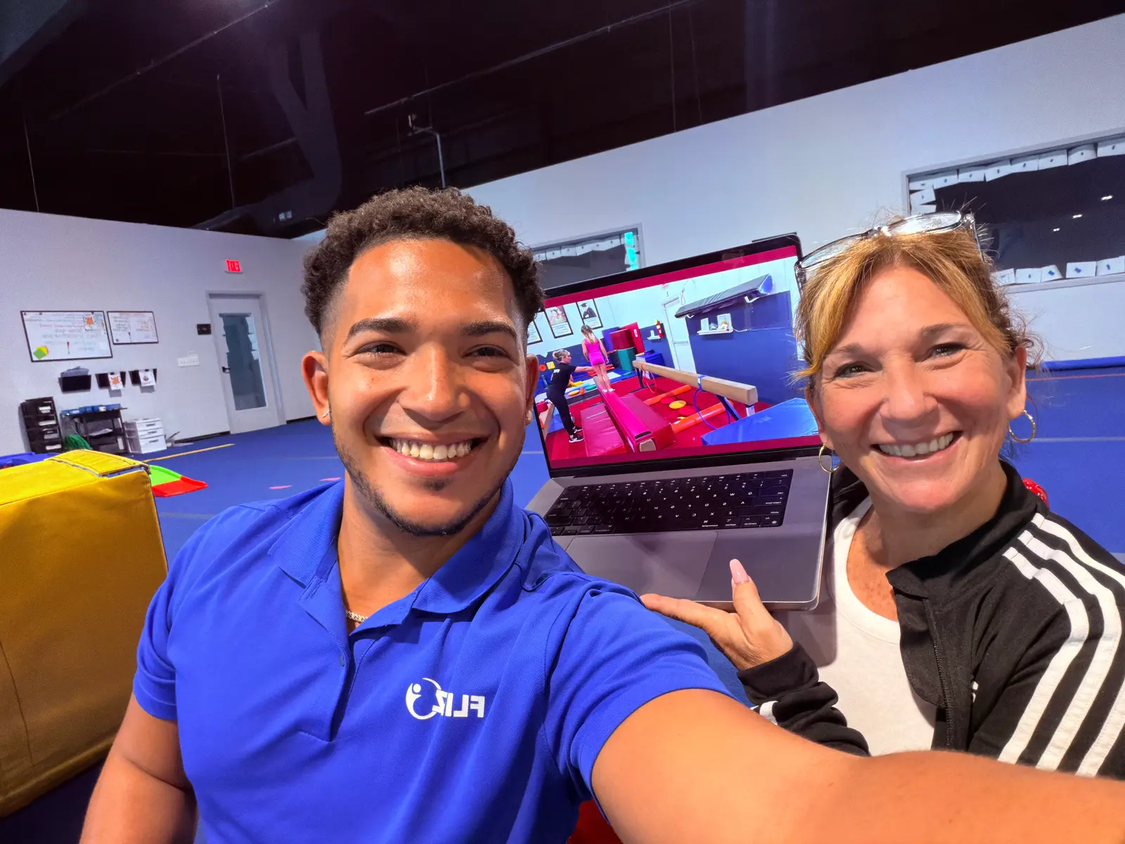 Two coaches on a gym floor with FlipBiz open on a laptop